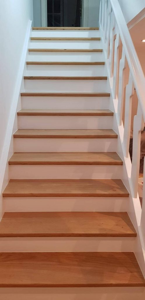 Dieselbe Treppe nach der Renovierung: aufgearbeitete Holzstufen, weiße Setzstufen, Wange und Wand